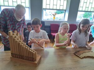 Three children building an Orgelkids kit. An old salt stands by to supervise.